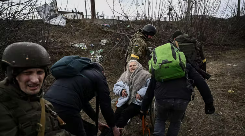 Pessoas ajudam uma idosa em cadeira de rodas a fugir de Irpin, Ucrânia, em 7 de março de 2022. Aris Messinis/AFP via Getty Images
